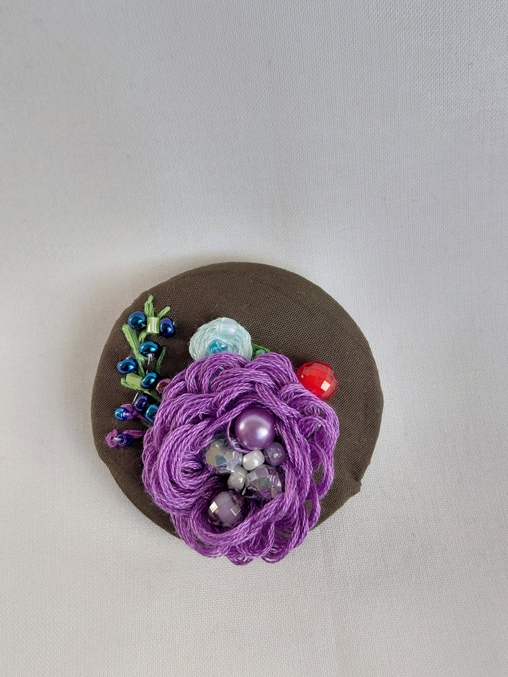 Decorative purple flower brooch on olive background