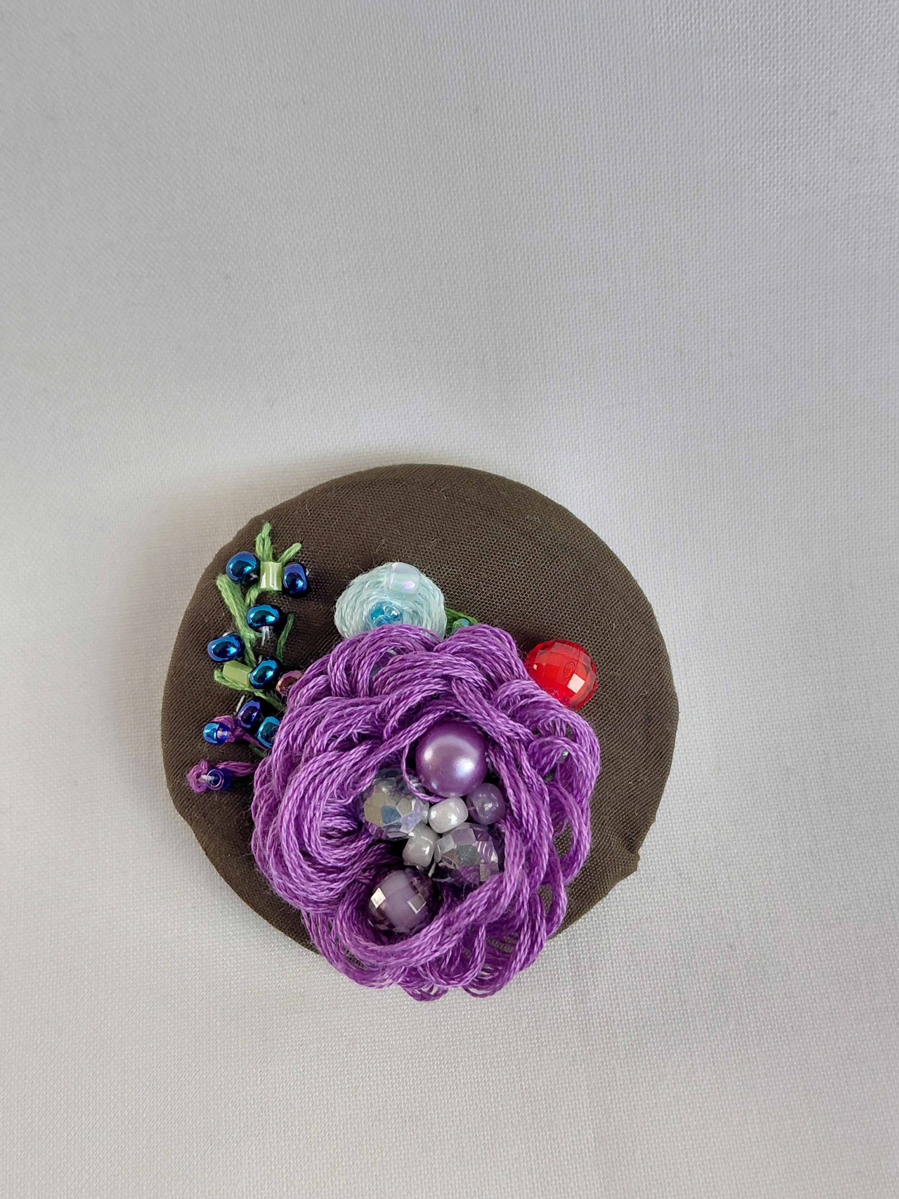 Decorative purple flower brooch on olive background