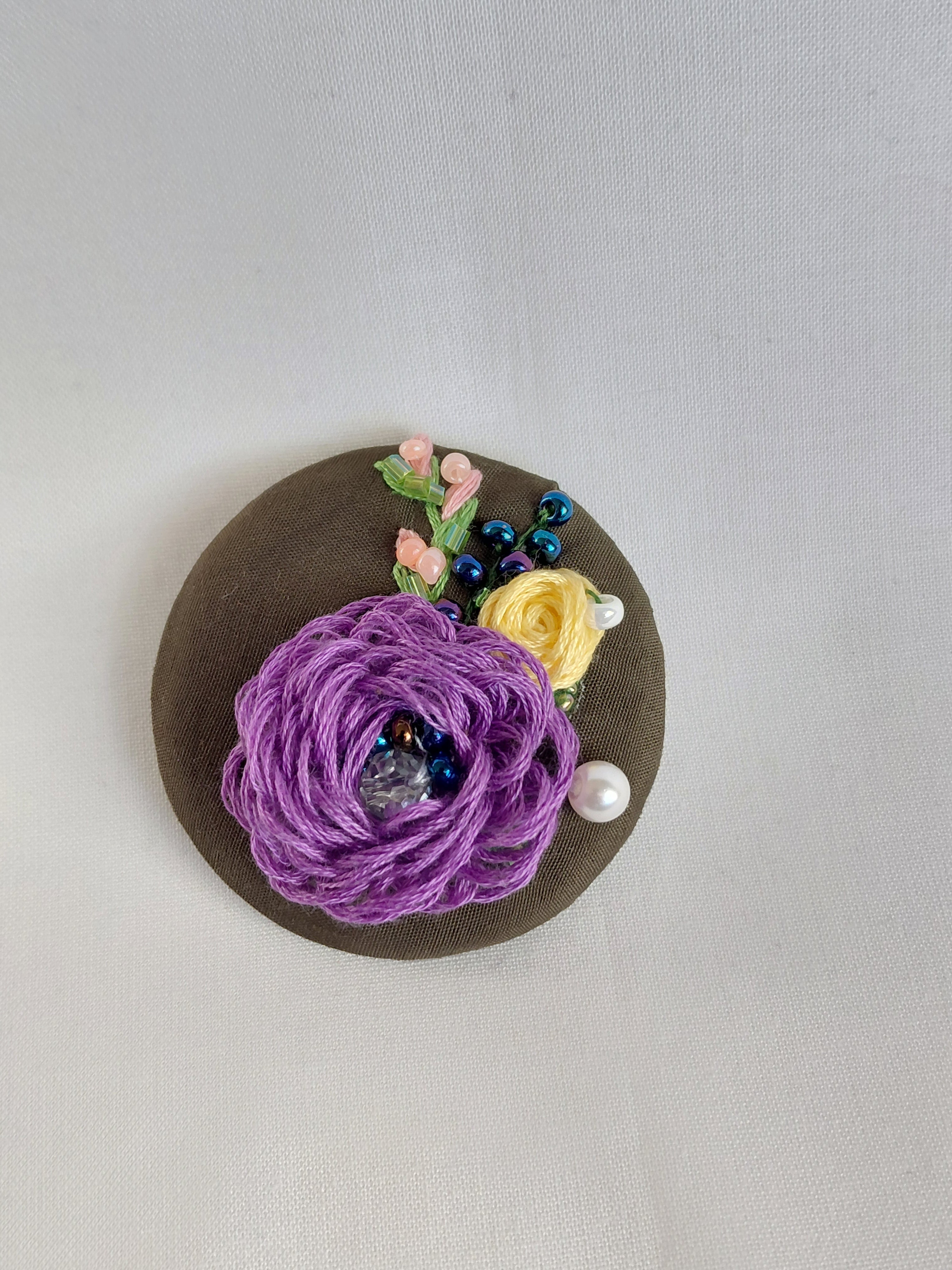 Decorative purple flower brooch on olive background