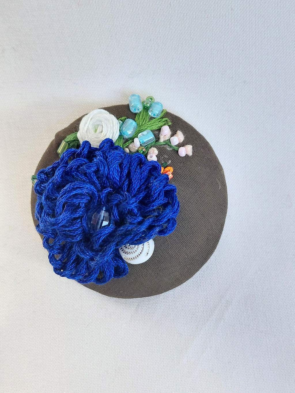Decorative blue flower brooch on olive background