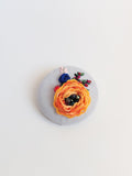 Decorative orange flower brooch on light blue background