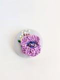 Decorative purple flower brooch on light blue background