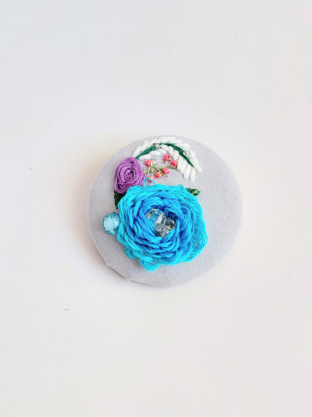 Decorative turquoise flower brooch on light blue background