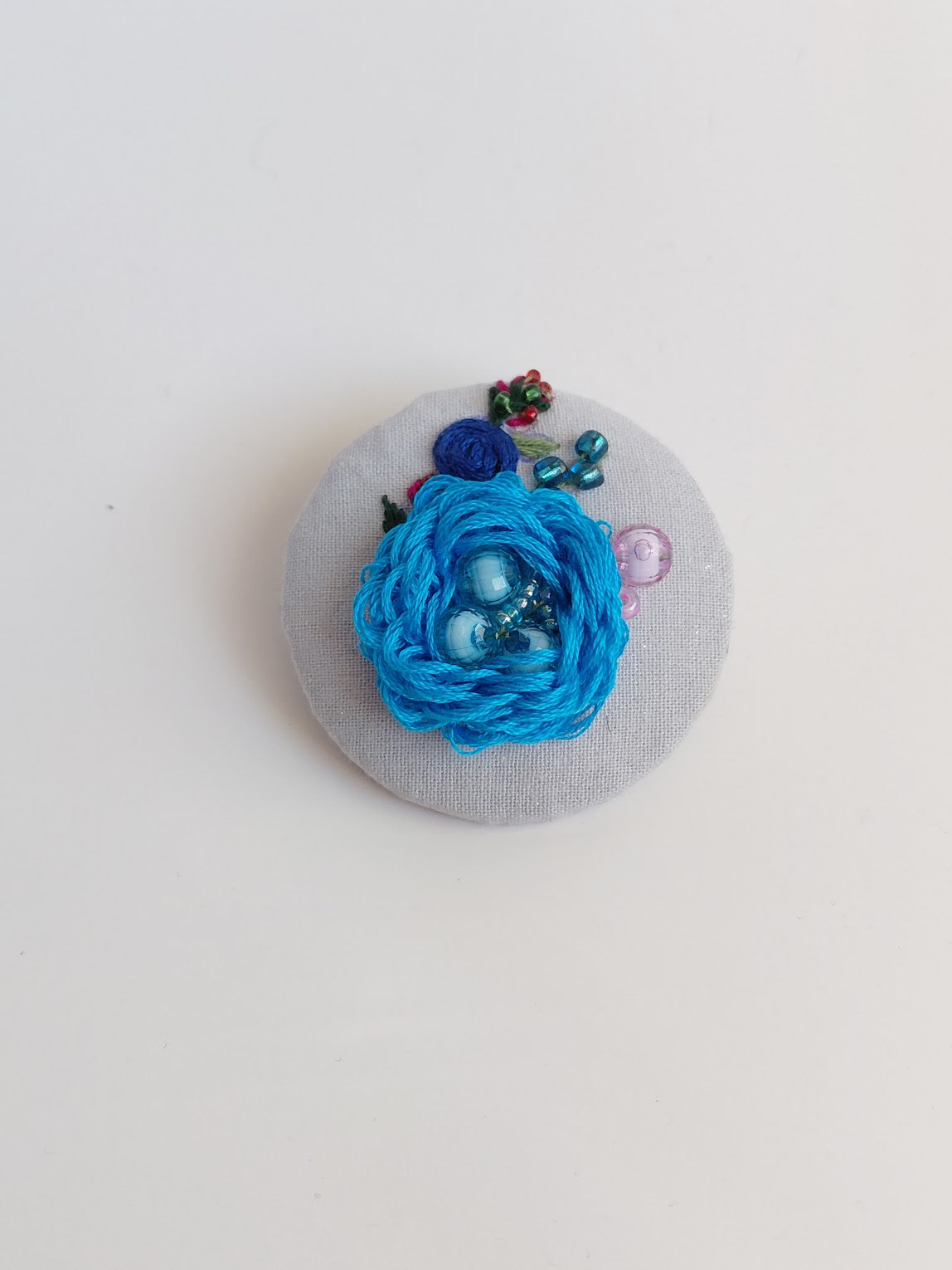 Decorative turquoise flower brooch on light blue specs background