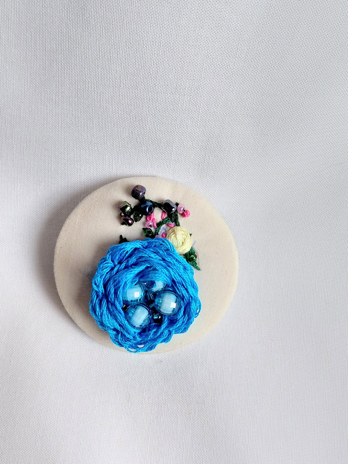 Decorative turquoise flower brooch on cream background