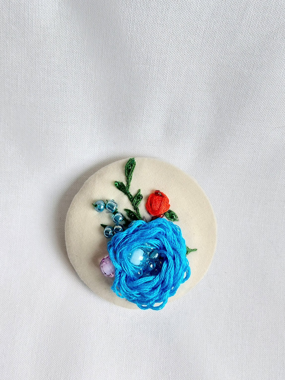 Decorative turquoise flower brooch on cream background