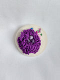 Decorative purple flower brooch on cream background